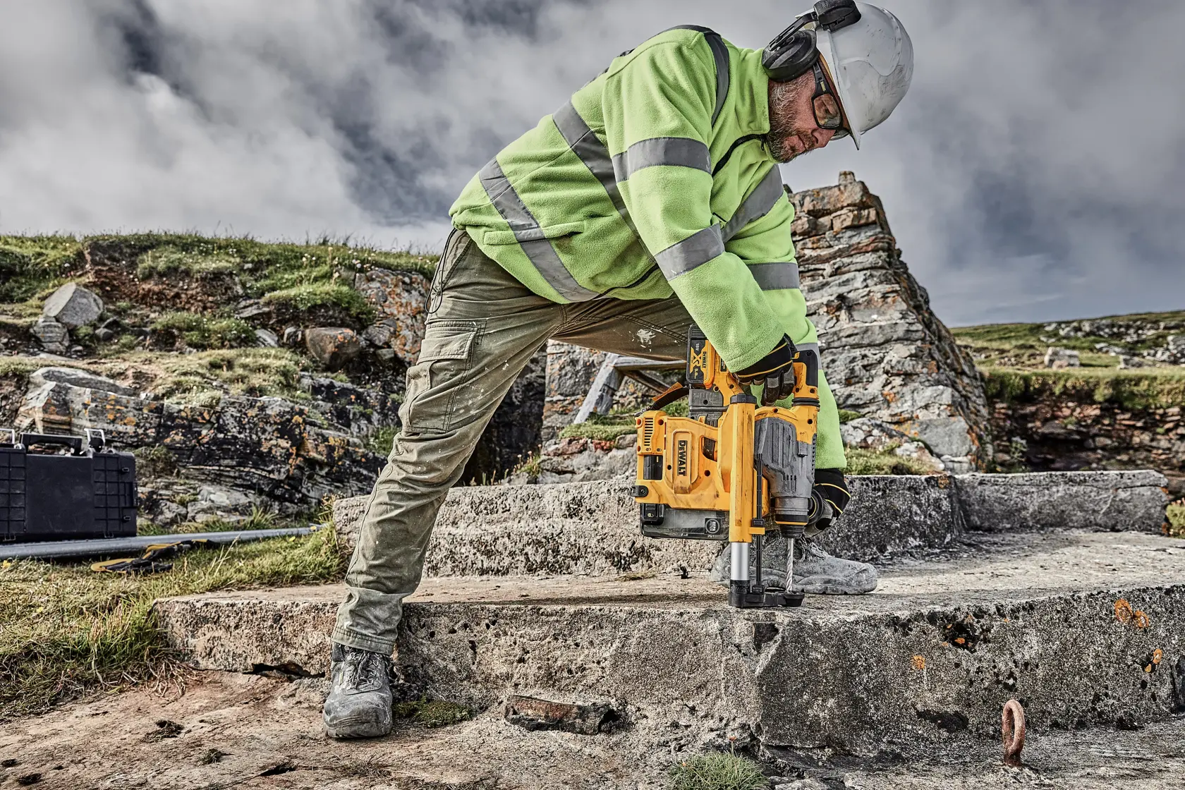 Foto de trabajador usando taladro DEWALT D25304DH en concreto al aire libre, con equipo de seguridad.