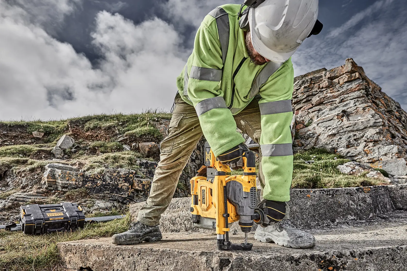 Foto de trabajador usando DEWALT D25304DH martillo rotativo en exterior sobre concreto, con equipo de seguridad.