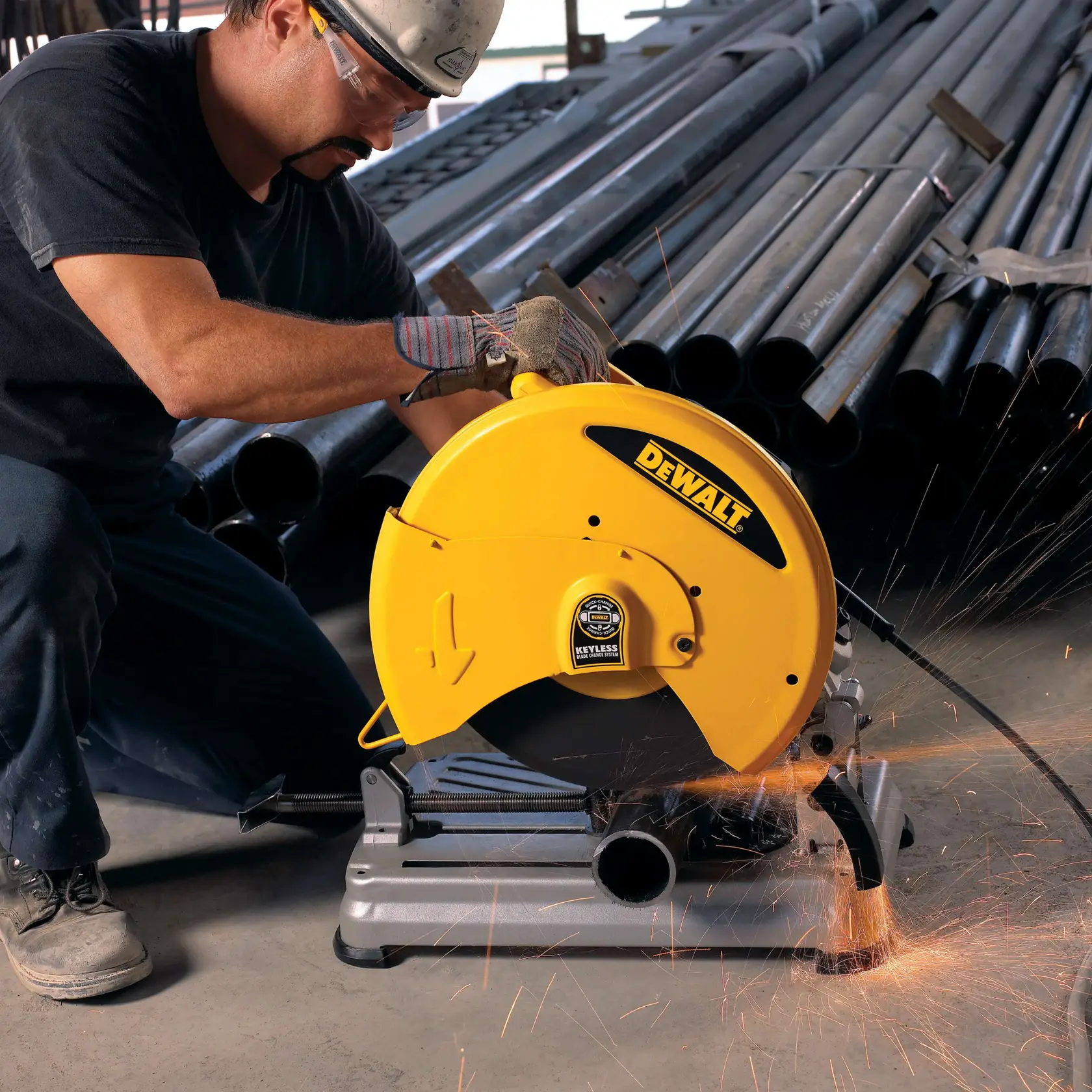 Un trabajador usa una sierra de corte de metal amarilla DEWALT D28715 para cortar una tubería de acero, con chispas volando, en un entorno industrial con tubos apilados al fondo.