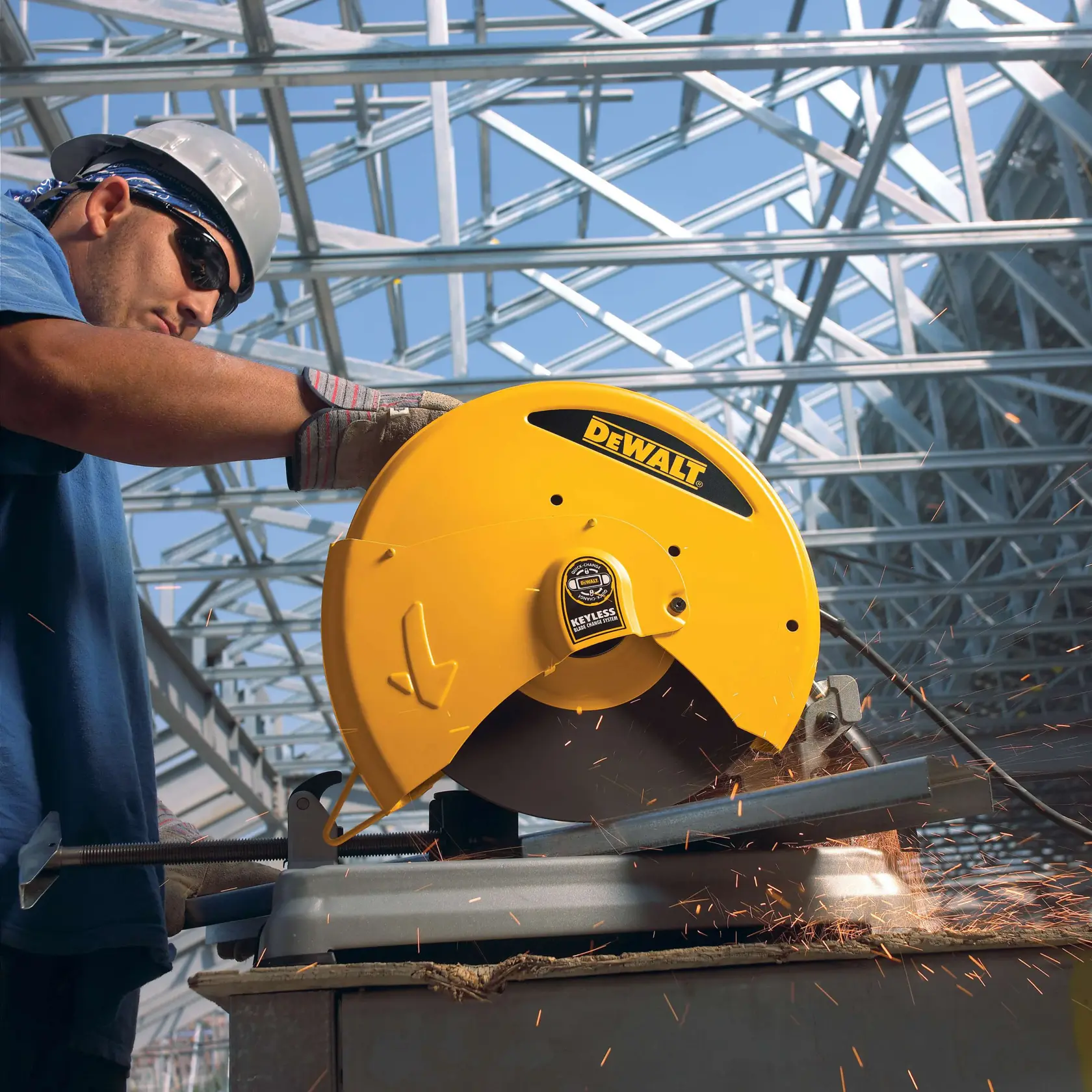 Una persona con guantes de trabajo y casco utiliza una sierra de corte DEWALT amarilla para cortar metal, mientras saltan chispas, dentro de un edificio con estructura de acero.