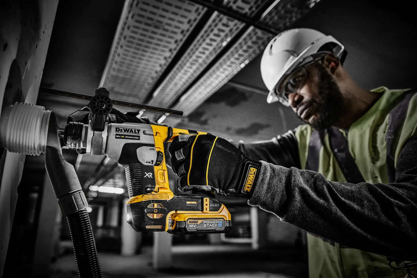 Trabajador perfora una pared con herramienta DEWALT PowerStack 18V, usando guantes y casco.