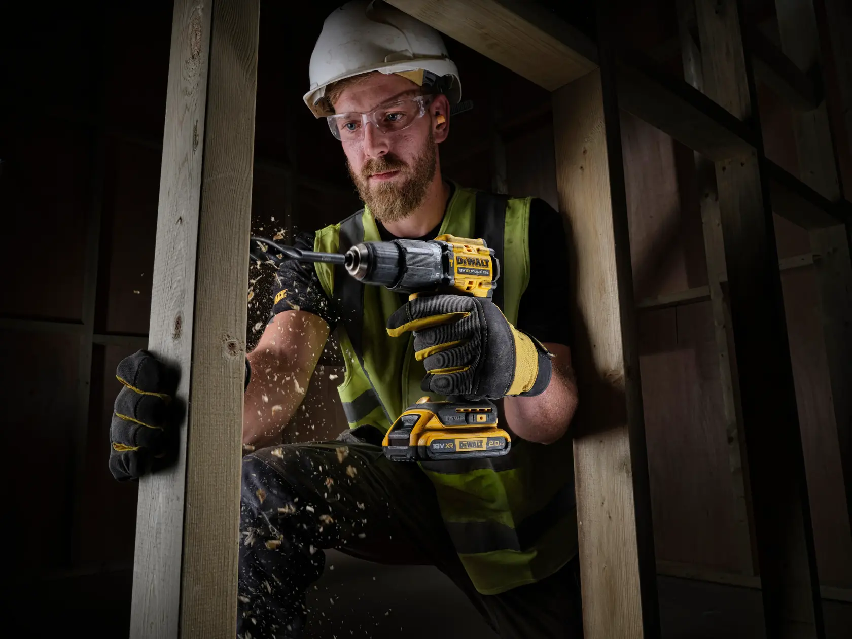 Trabajador perfora madera con taladro DEWALT inalámbrico, usando guantes y casco en obra.