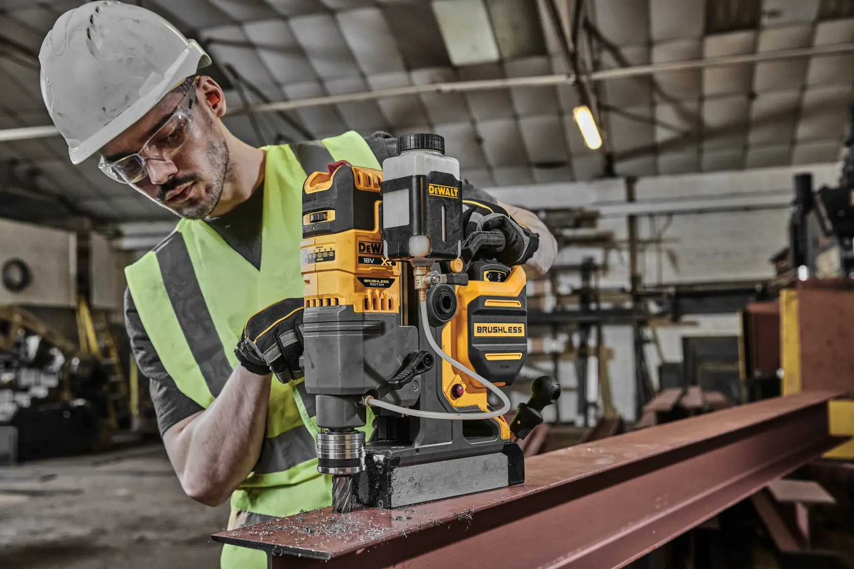 Taladro brushless DEWALT DCD1623N usado en viga metálica en taller, operado por persona con equipo de seguridad.