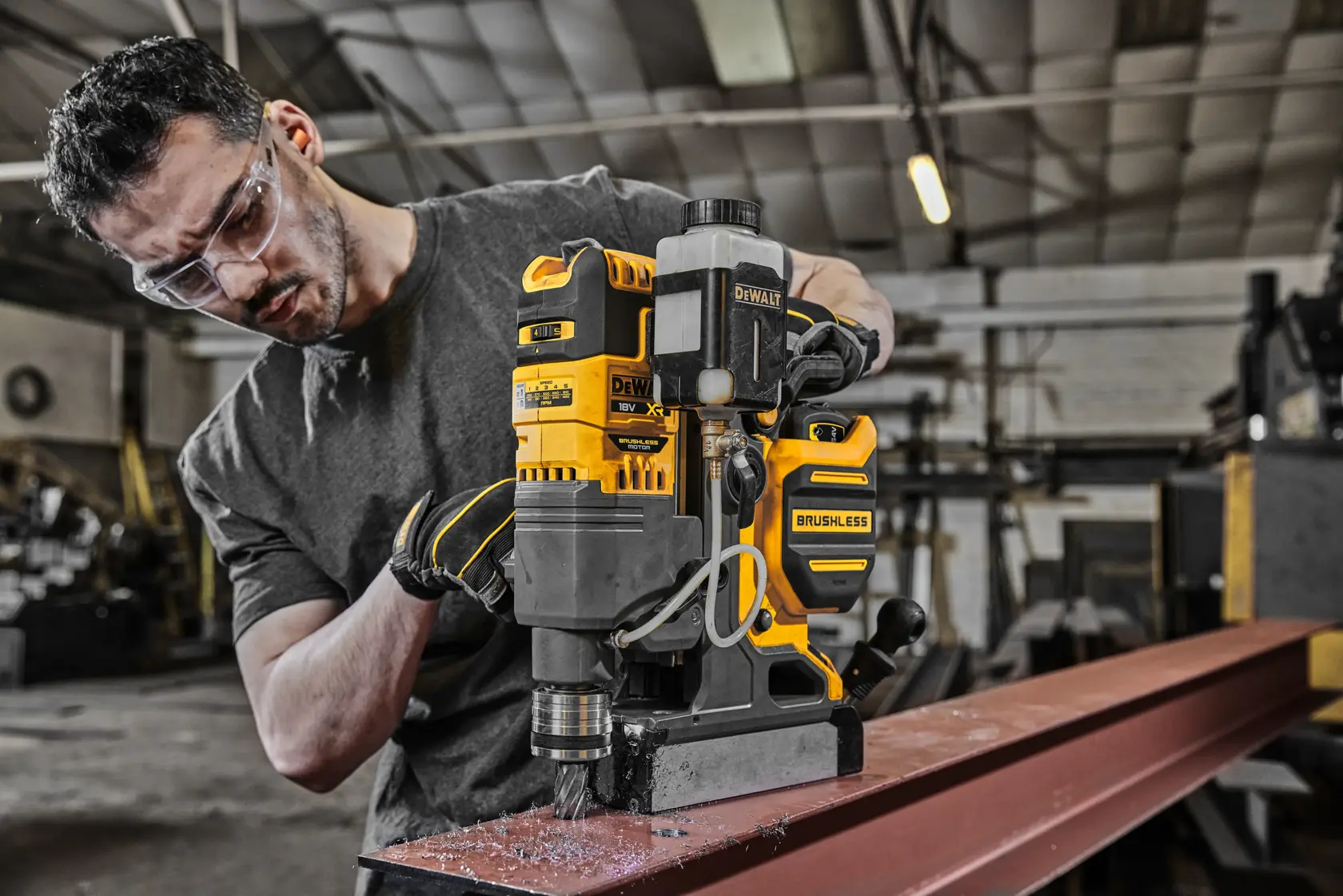 Taladro brushless DEWALT DCD1623N usado en viga de acero en taller por persona con rostro oculto.