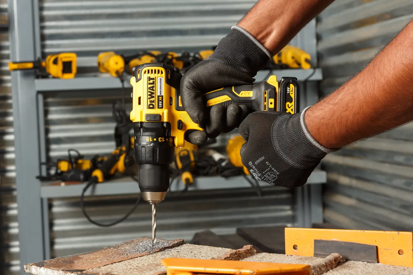 Manos con guantes usando taladro inalámbrico DEWALT en madera. Herramientas visibles al fondo.