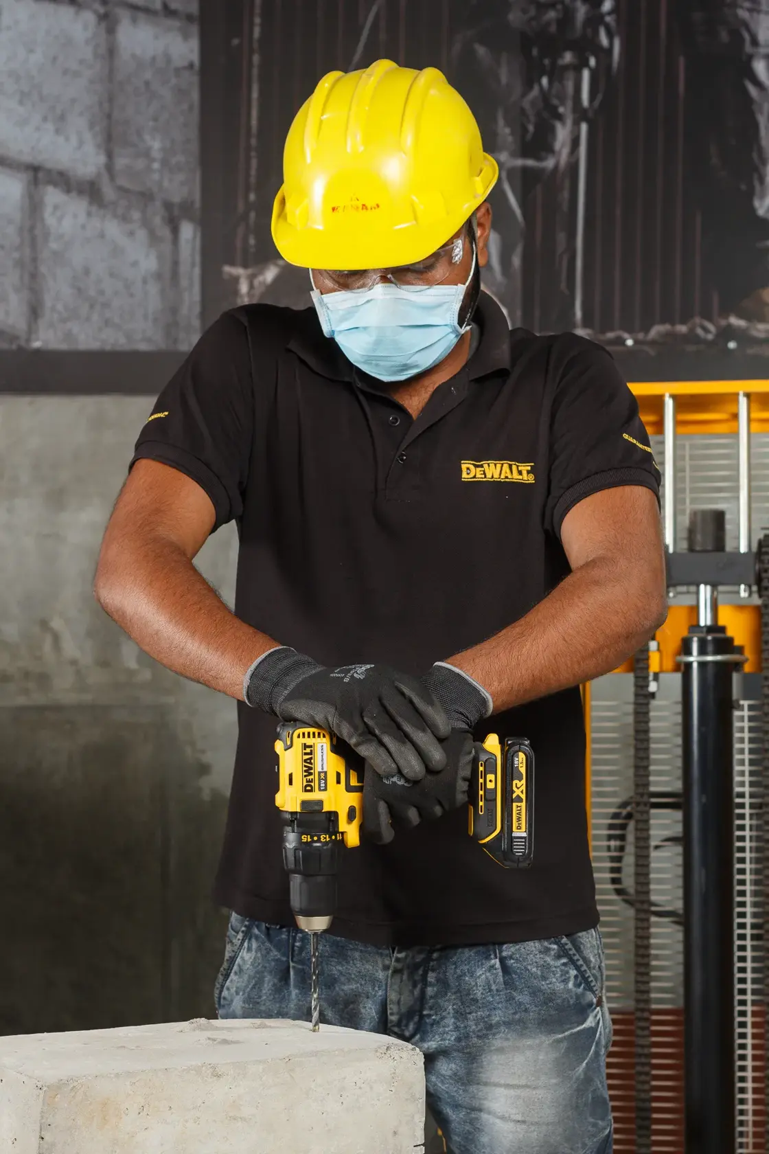 Persona con equipo de seguridad usa taladro inalámbrico DEWALT en concreto en obra.