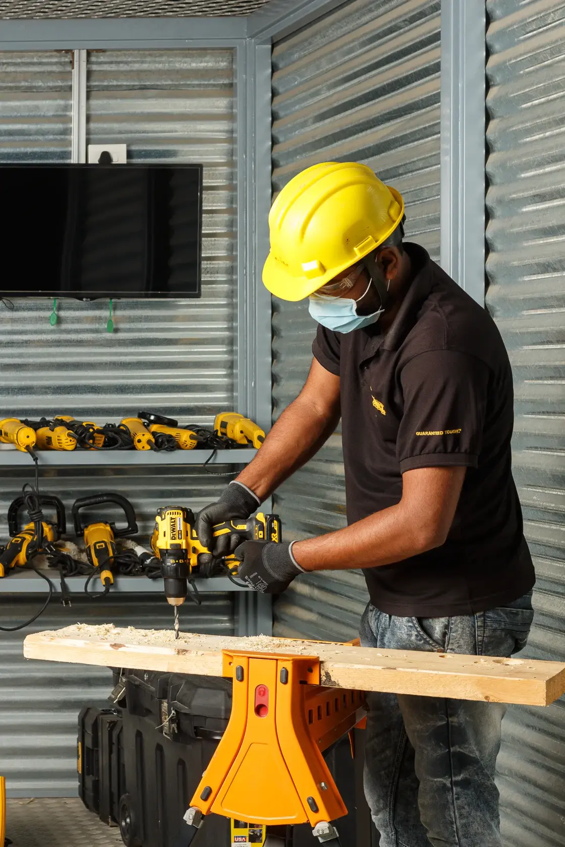 Persona con protección perfora madera con DEWALT DCD777S2T-QW, rodeada de herramientas DEWALT.