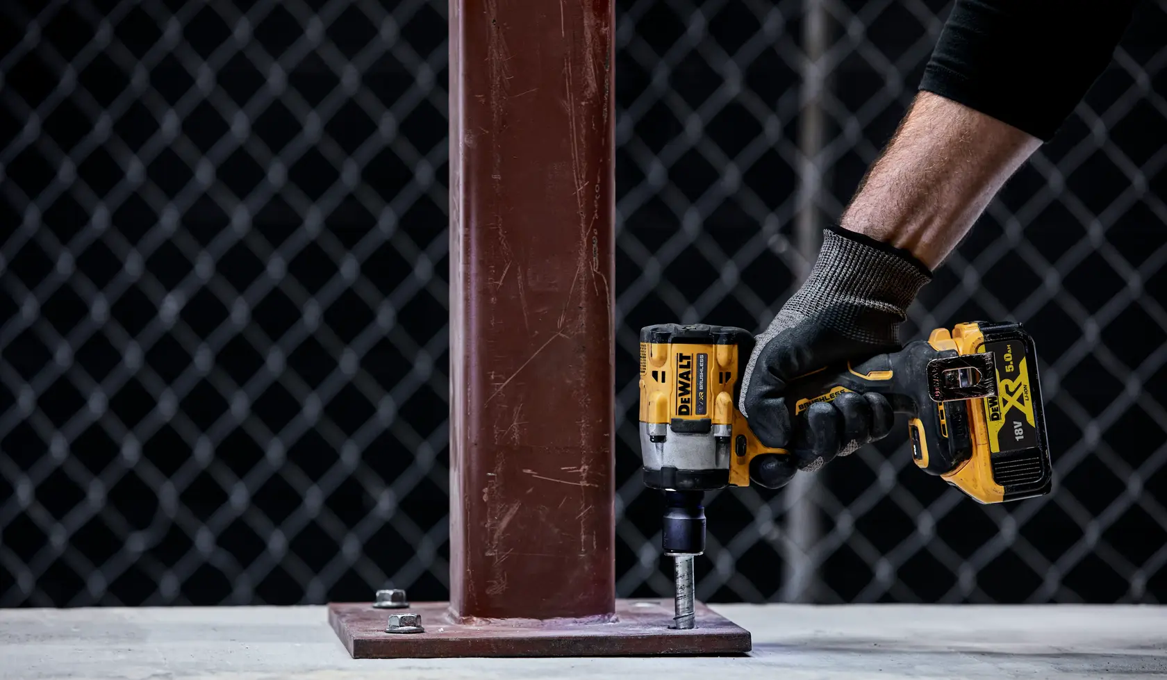 Foto de llave de impacto DEWALT DCF922P2T ajustando un perno en base metálica, trabajador con guantes.