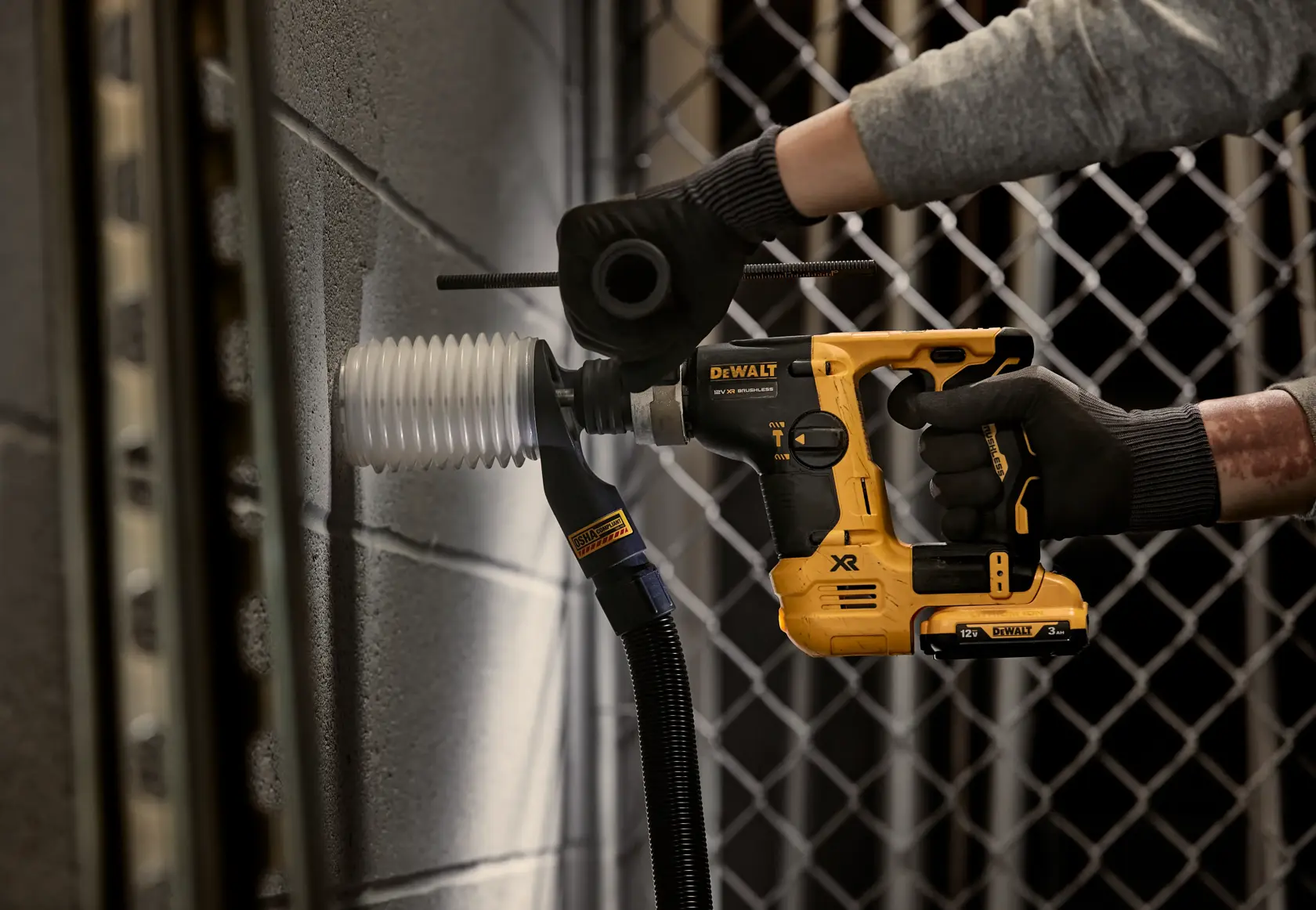 Persona usando un martillo rotativo DEWALT en pared de concreto junto a un conducto eléctrico.