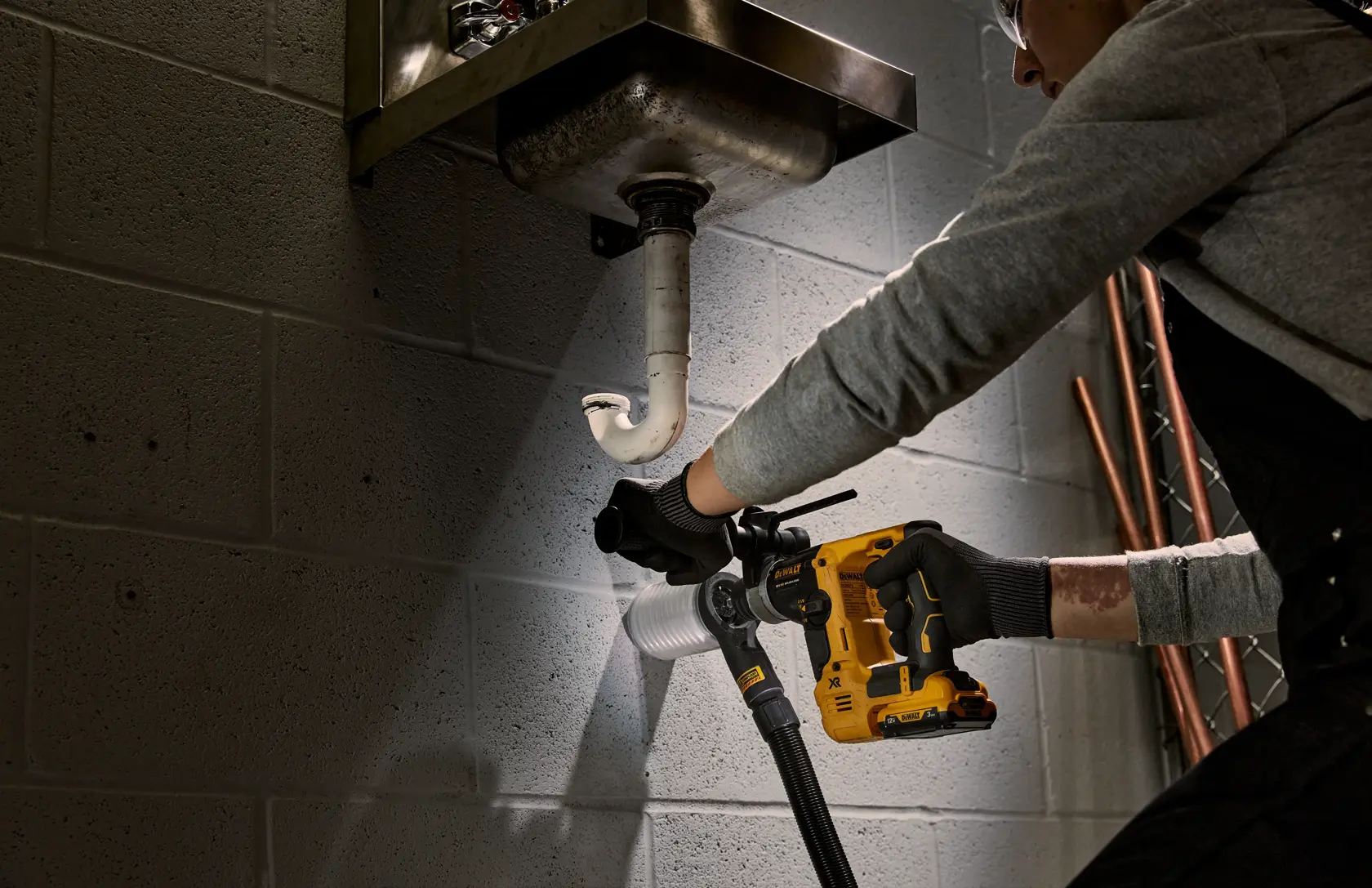 Persona usa un martillo rotativo DEWALT para perforar pared de cemento cerca de tuberías.