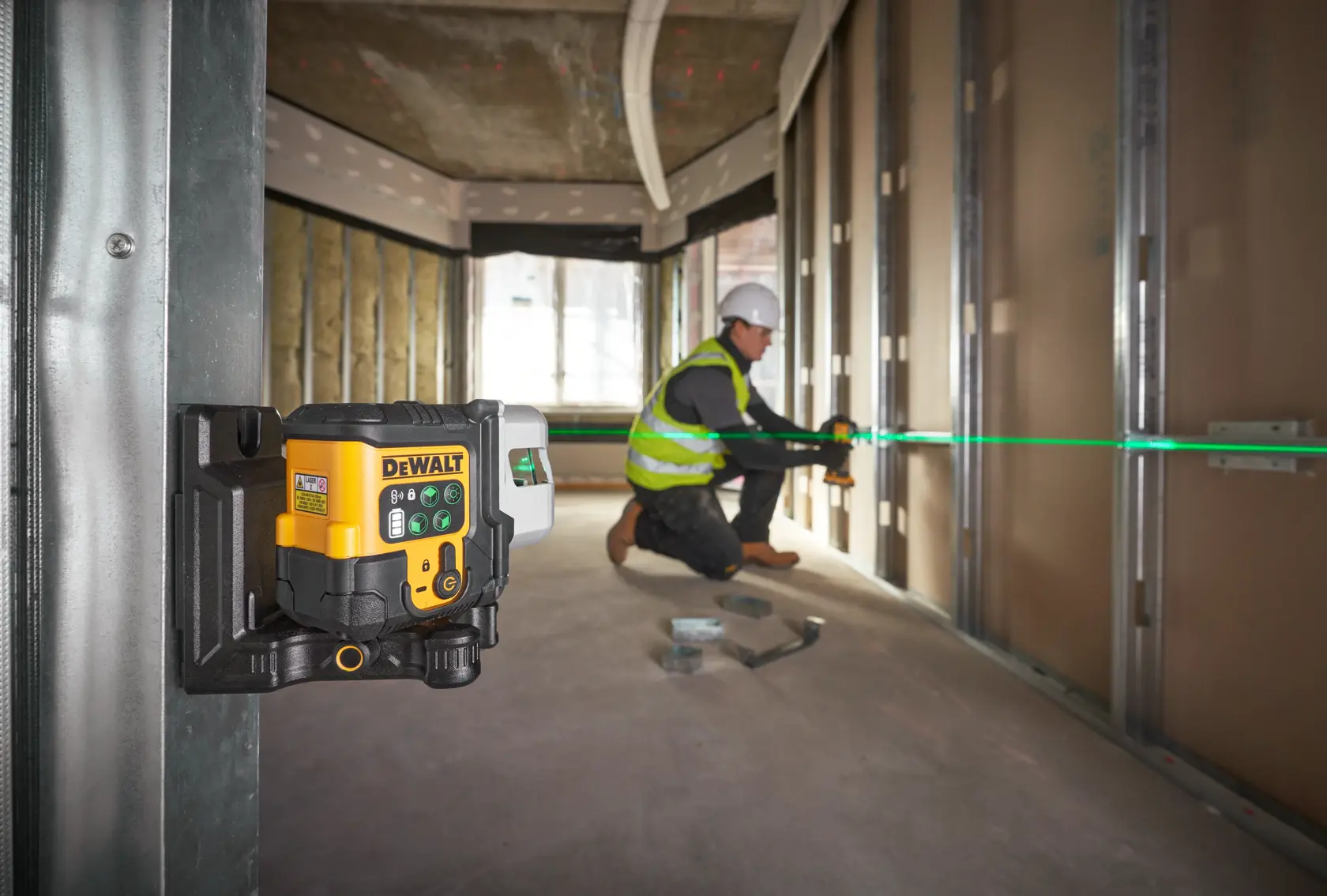 Nivel láser DEWALT con línea verde, usado por un trabajador para alinear paredes en una obra.