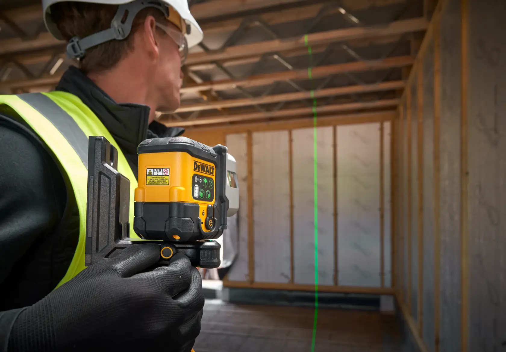 Trabajador usa nivel láser verde DEWALT para alinear en edificio en construcción.