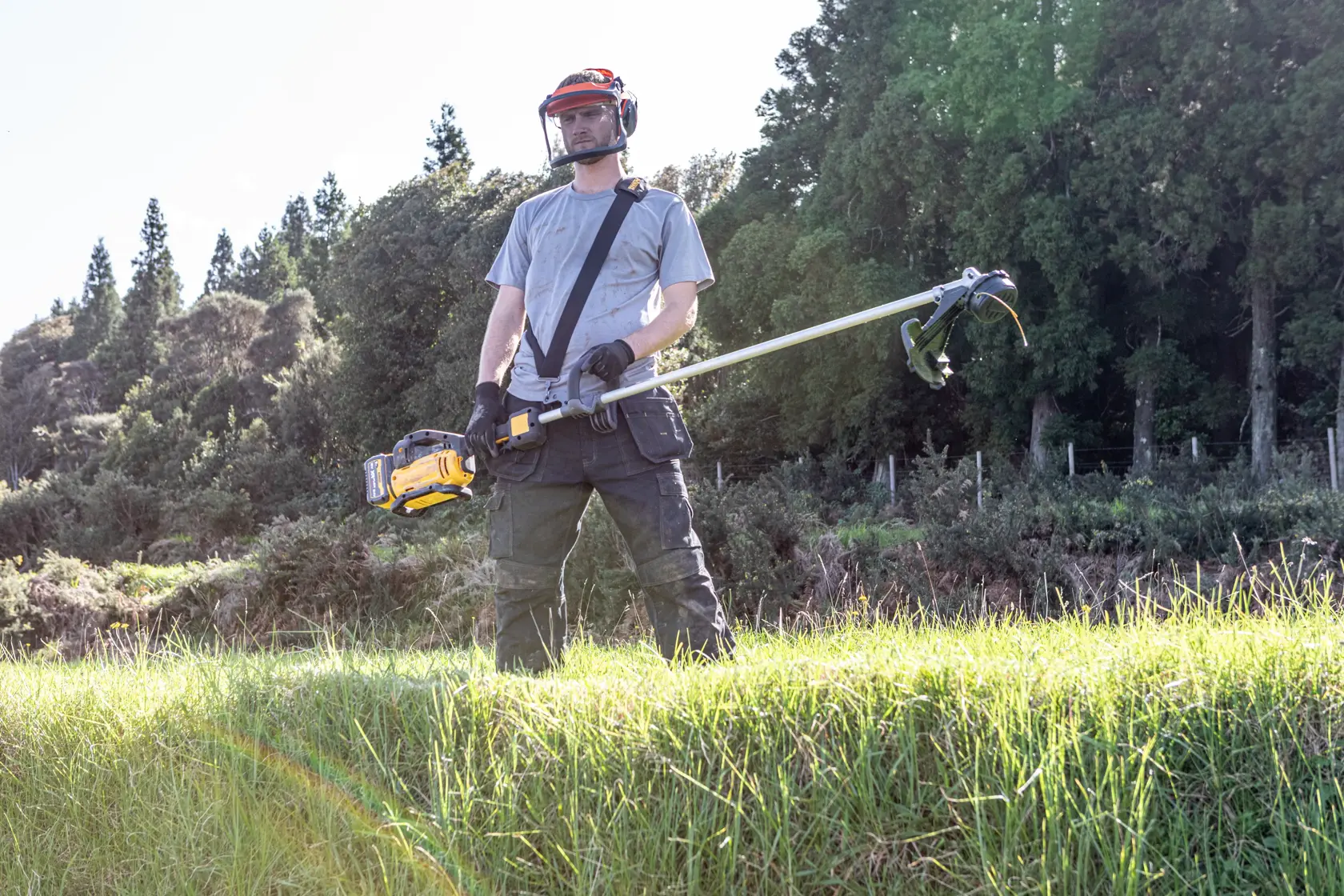 Persona con equipo de protección usa desbrozadora DEWALT DCMST911N y DCMST911N-XJ al aire libre.