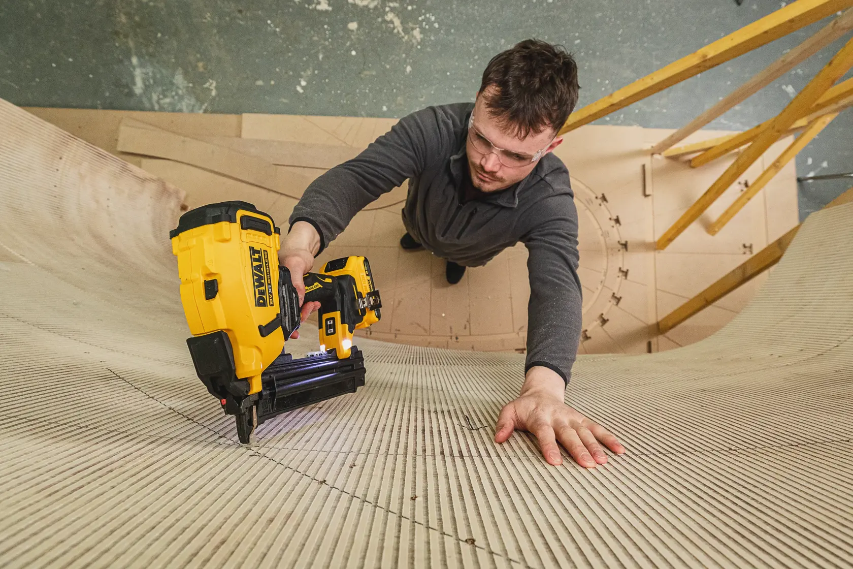 Persona usando clavadora DEWALT DCN210SN-XJ para fijar paneles de madera curvos en un taller.