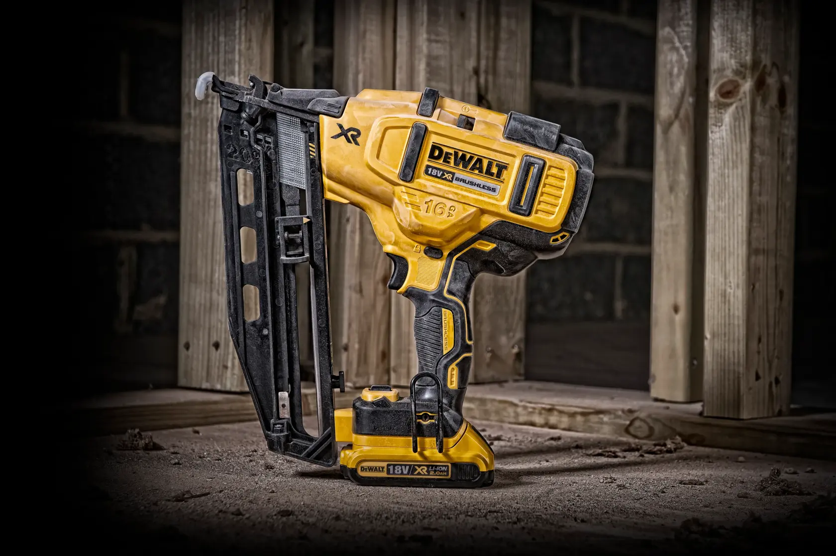 Clavadora inalámbrica DEWALT 18V sobre suelo polvoriento junto a vigas de madera en obra.