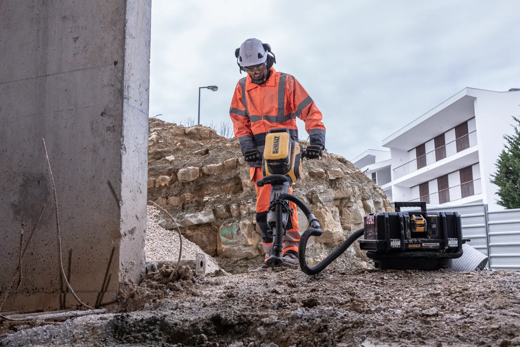 Persona usa herramienta DEWALT en obra exterior, con ropa de seguridad naranja y casco.