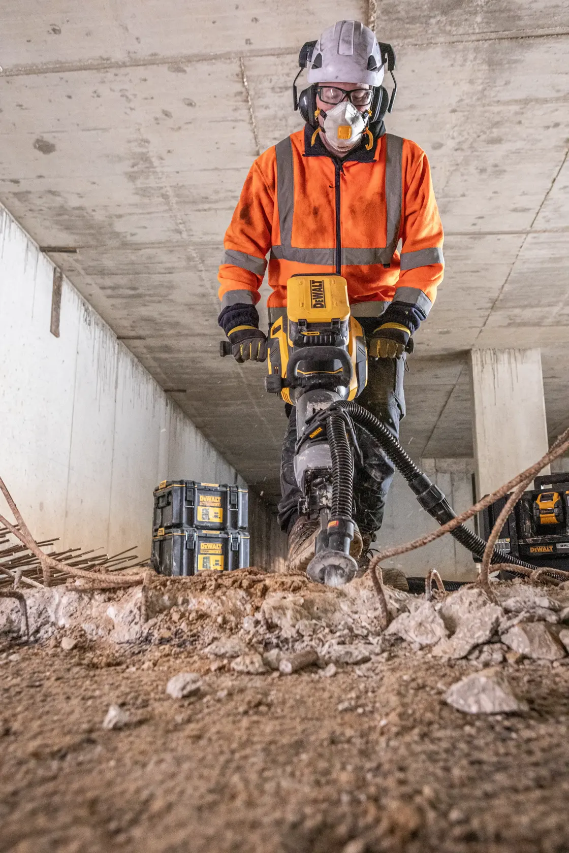 Trabajador usa DEWALT DCPS966N en concreto, equipo de seguridad y cajas de herramientas visibles.