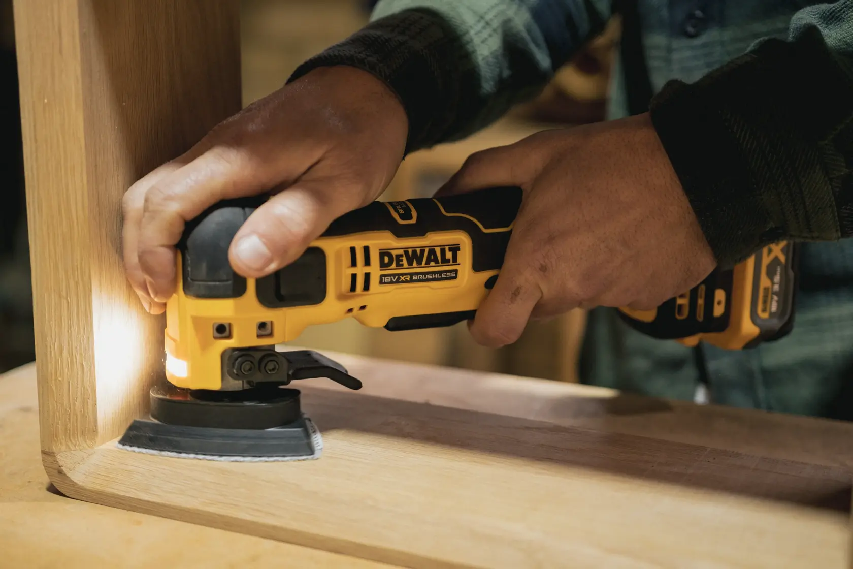 Persona lija una esquina de mueble de madera con herramienta multifunción inalámbrica DEWALT.
