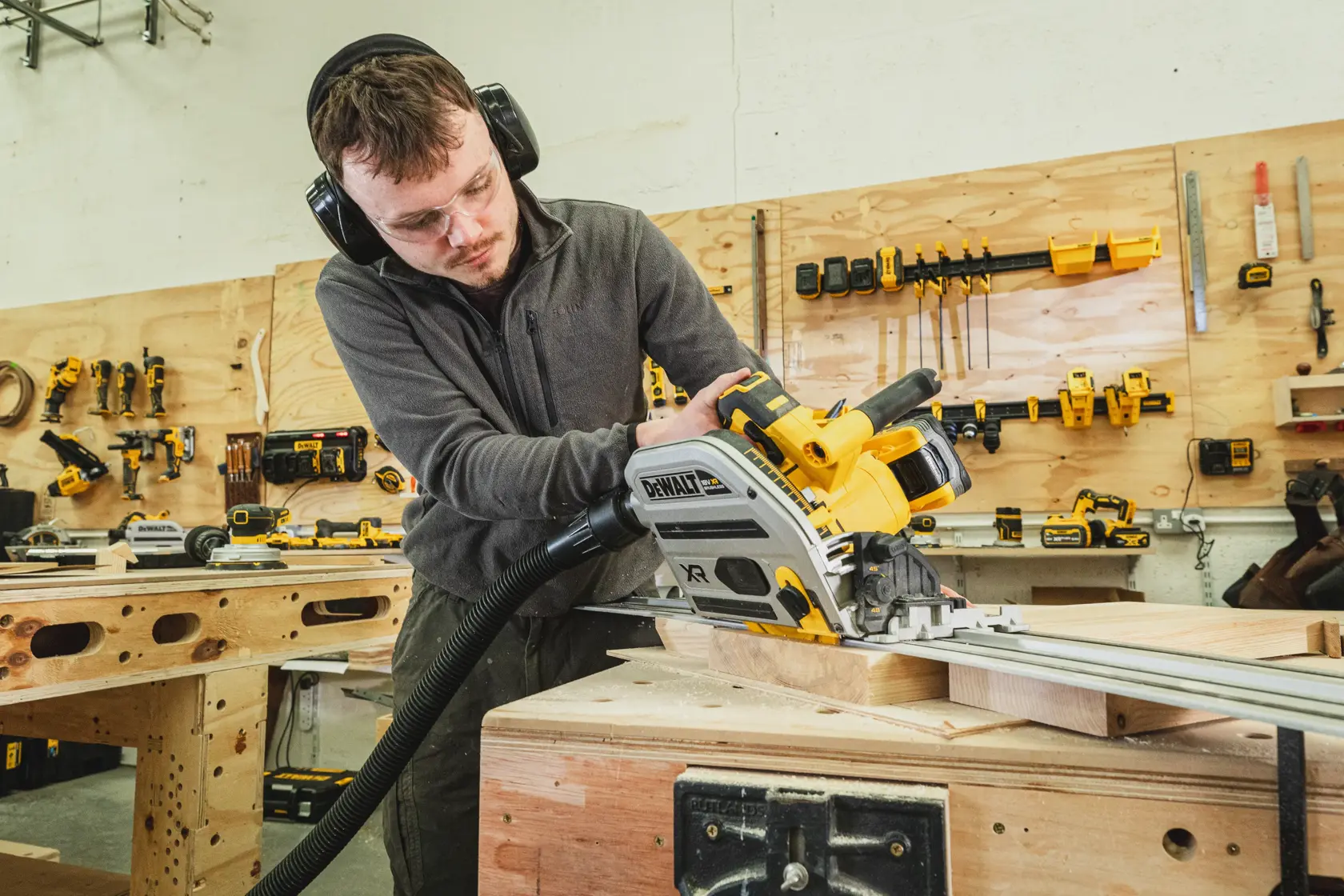 Persona usa una sierra de carril DEWALT inalámbrica en madera, en taller, con protección.