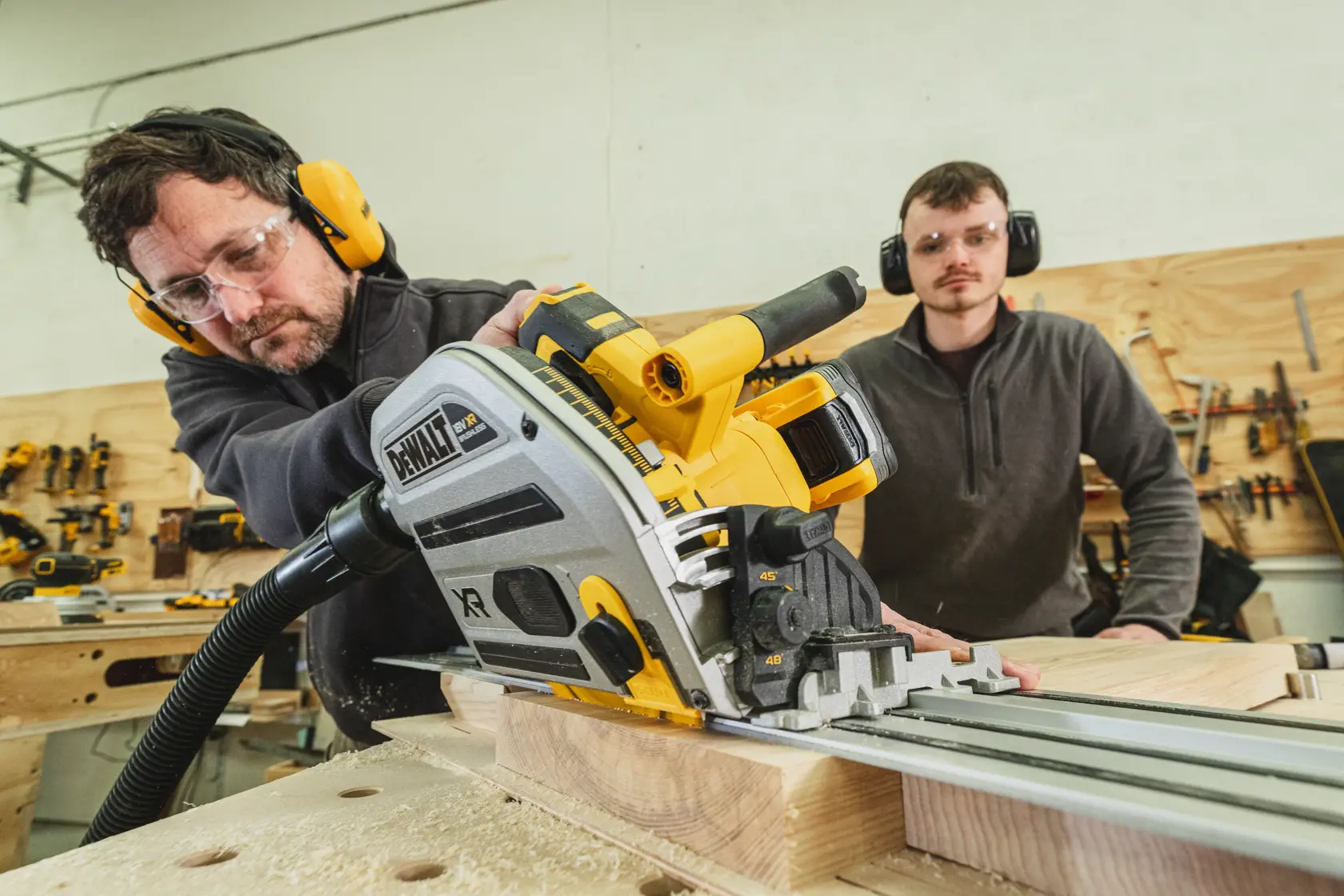Hombre usa una sierra de carril DEWALT para cortar madera, otra persona observa en el taller.