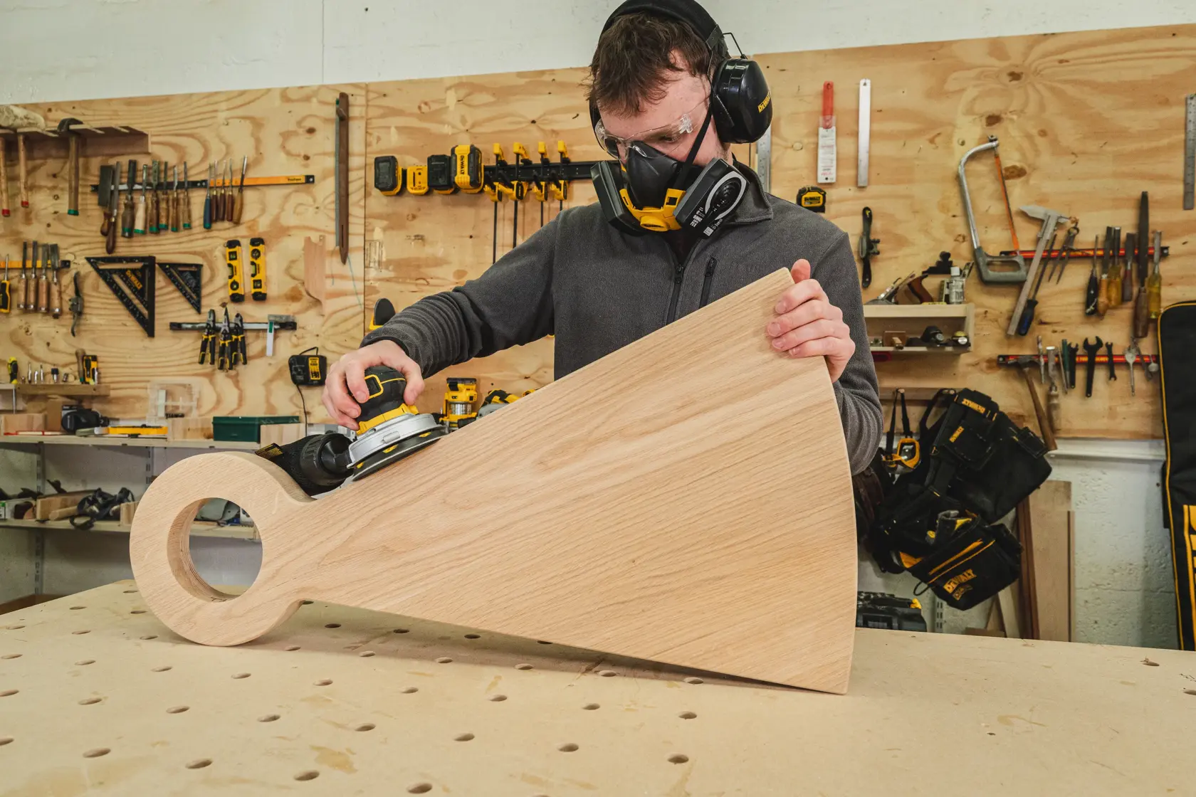 Persona usando una lijadora DEWALT en una pieza grande de madera en un taller.
