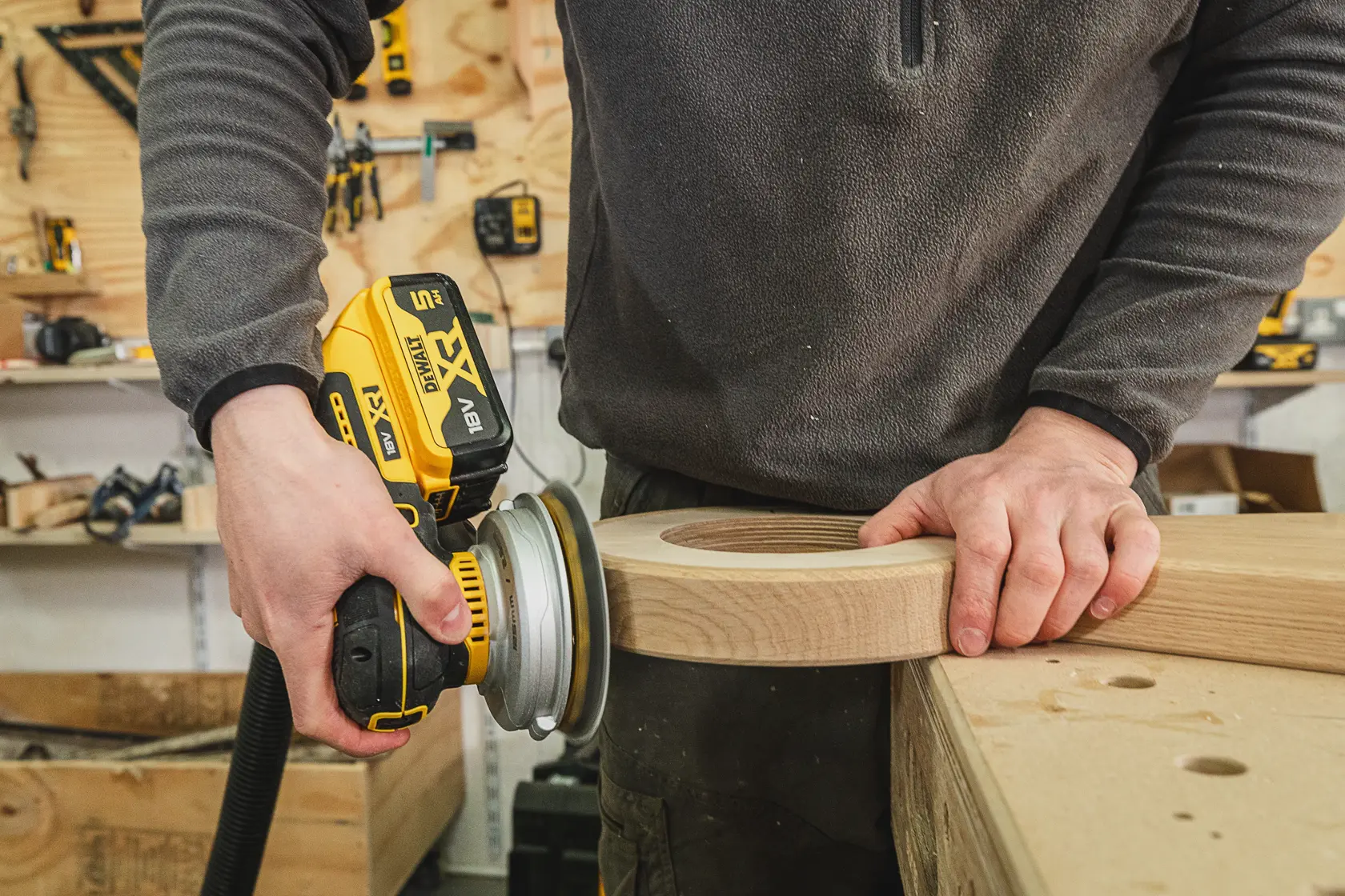 Persona usa una lijadora inalámbrica DEWALT para suavizar madera en taller.