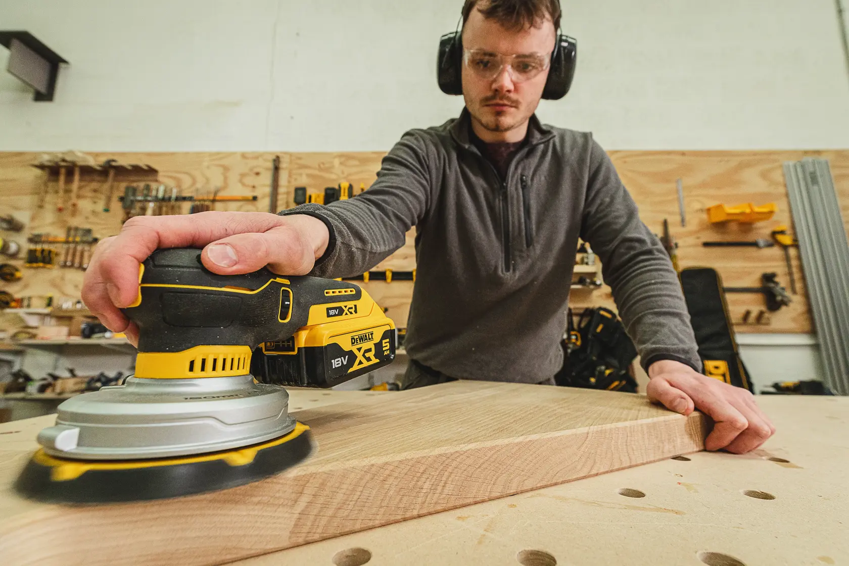 Persona lijando madera con una lijadora inalámbrica DEWALT DCW230N-XJ en un taller.
