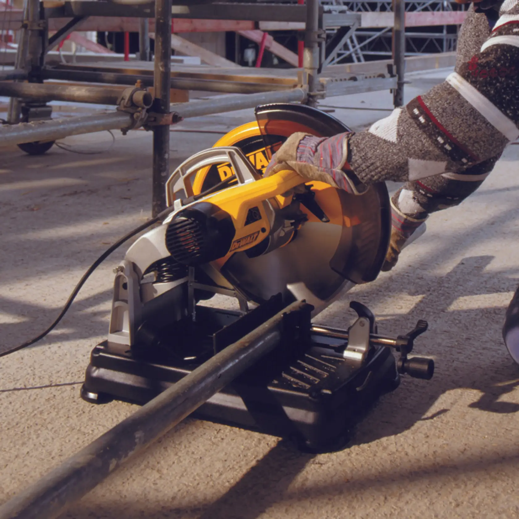 Trabajador corta tubo de metal con DEWALT DT1922 en obra, utilizando guantes para seguridad.