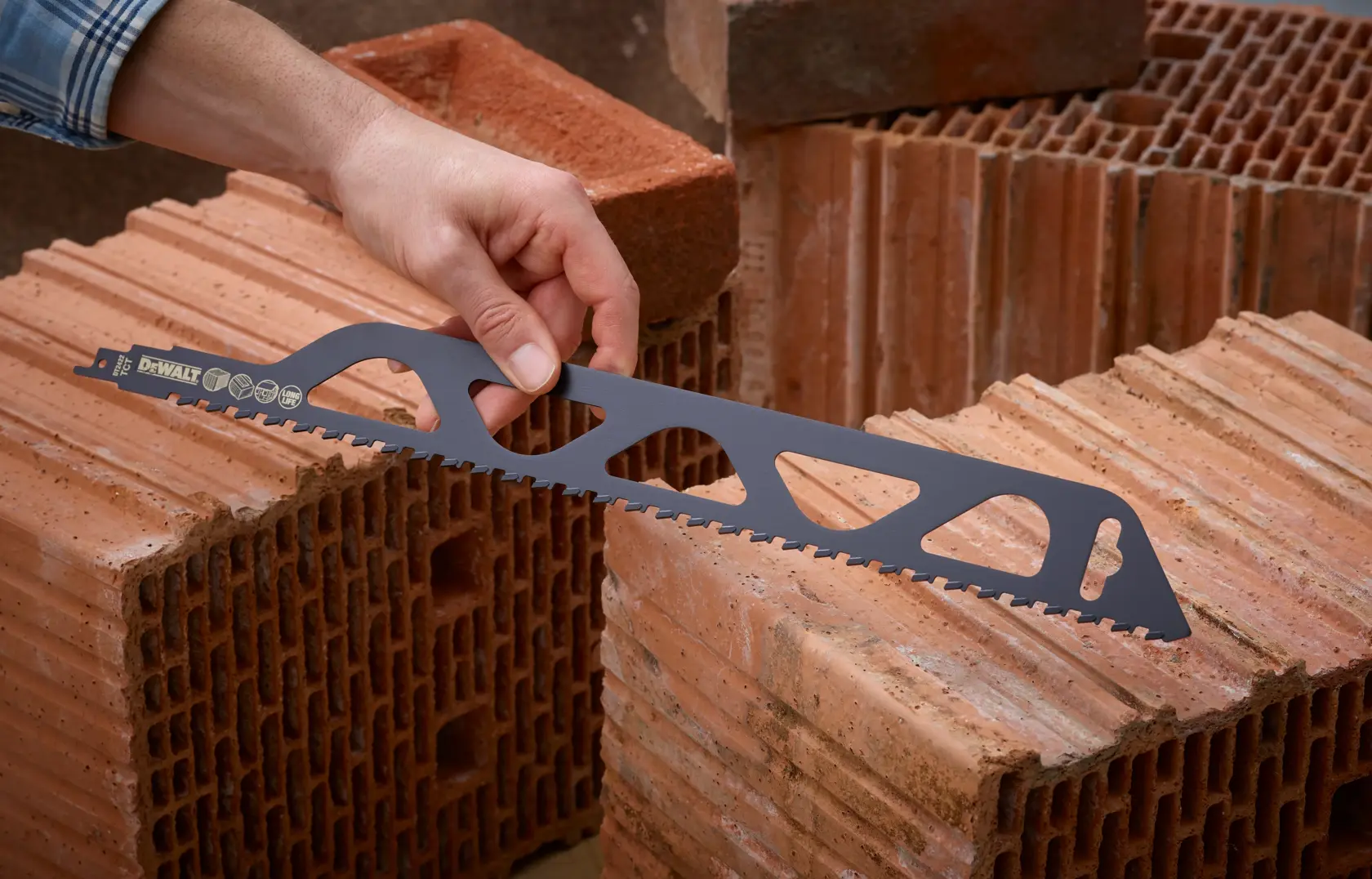 Persona sostiene hoja de sierra DEWALT para ladrillos sobre bloques huecos en ambiente de construcción.