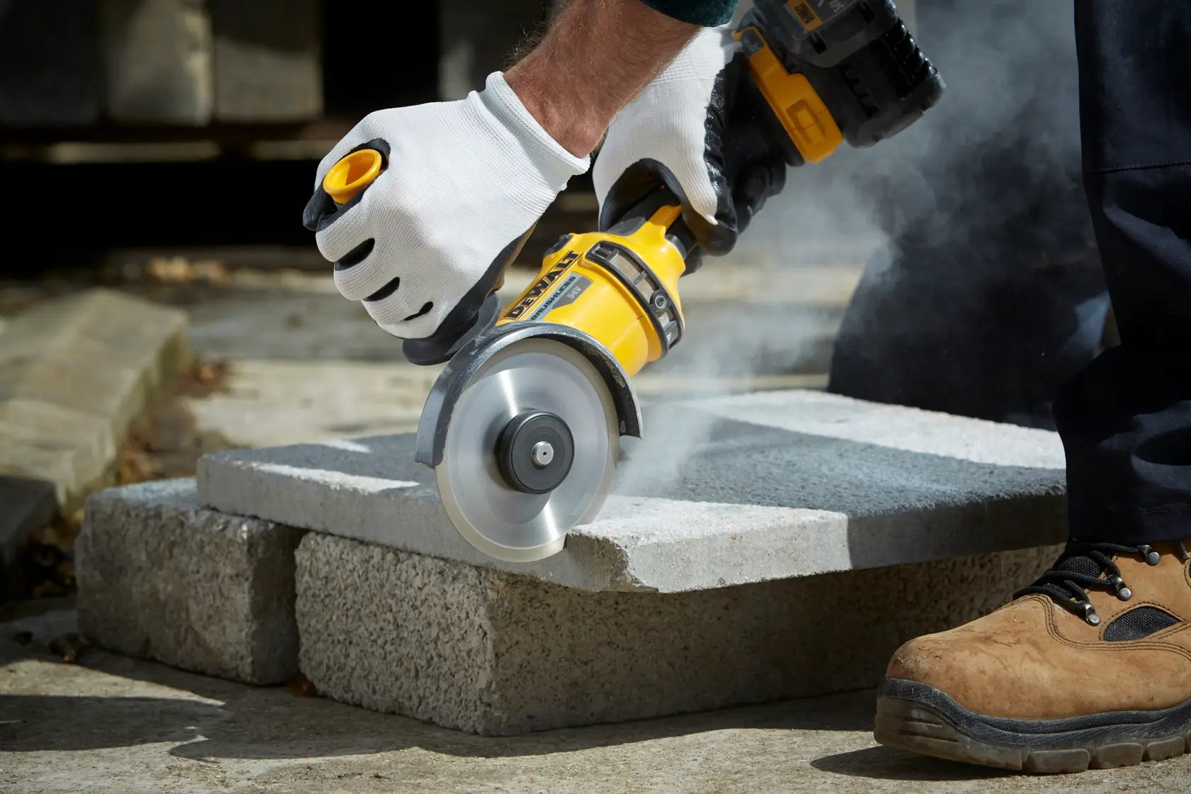 Persona corta bloque de hormigón con esmeriladora DEWALT DT3711 al aire libre, usando guantes y calzado de seguridad.