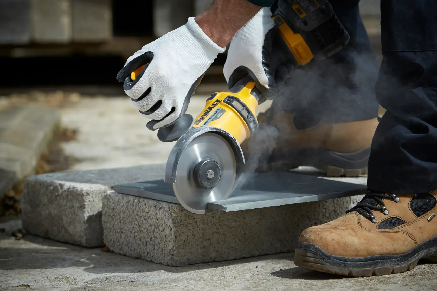 Persona corta piedra al aire libre con amoladora DEWALT, usando guantes y botas de seguridad.