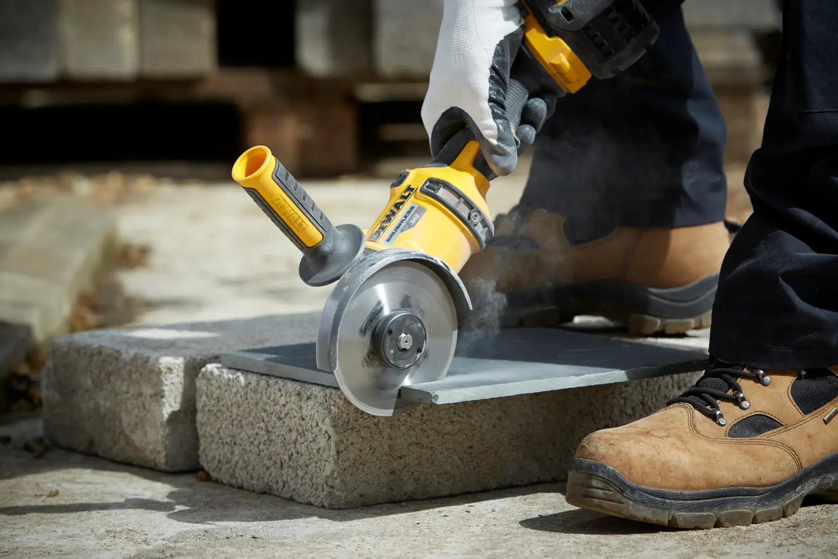 Persona corta una losa de piedra con una amoladora DEWALT, usando guantes y calzado de seguridad.