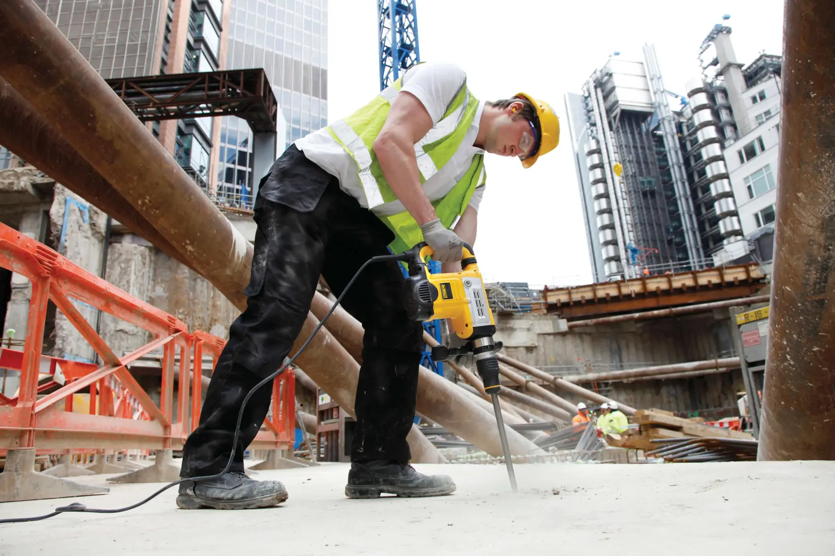 Trabajador perfora concreto en obra con DEWALT DT6824, edificios visibles al fondo.