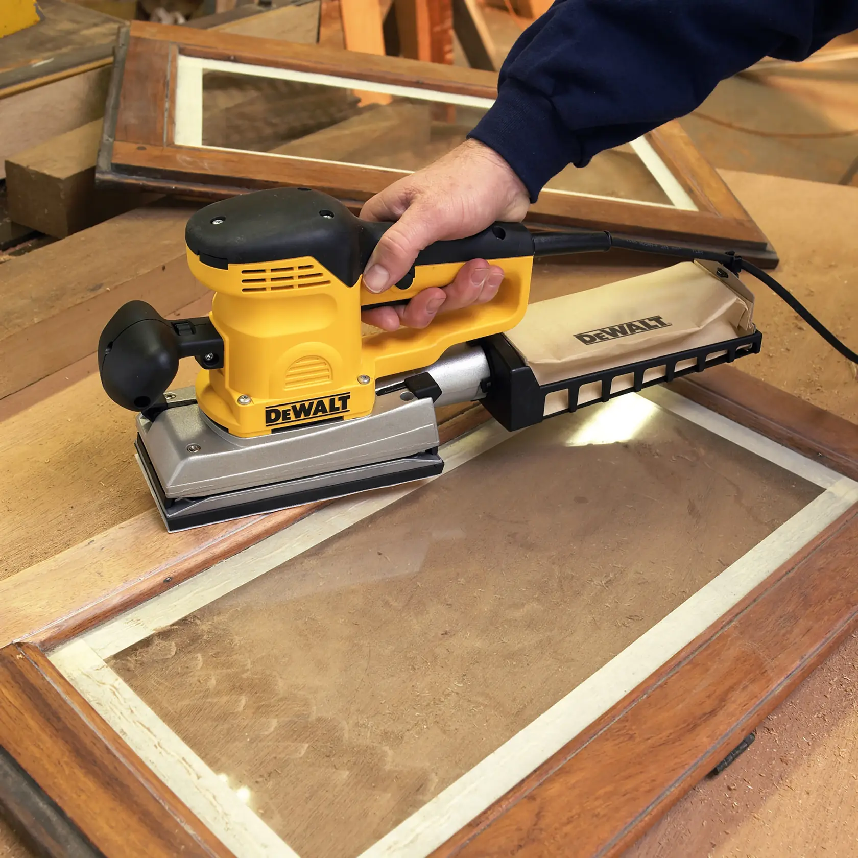 Lijadora DEWALT DT8592 usada en marco de ventana de madera, bolsa de polvo visible.