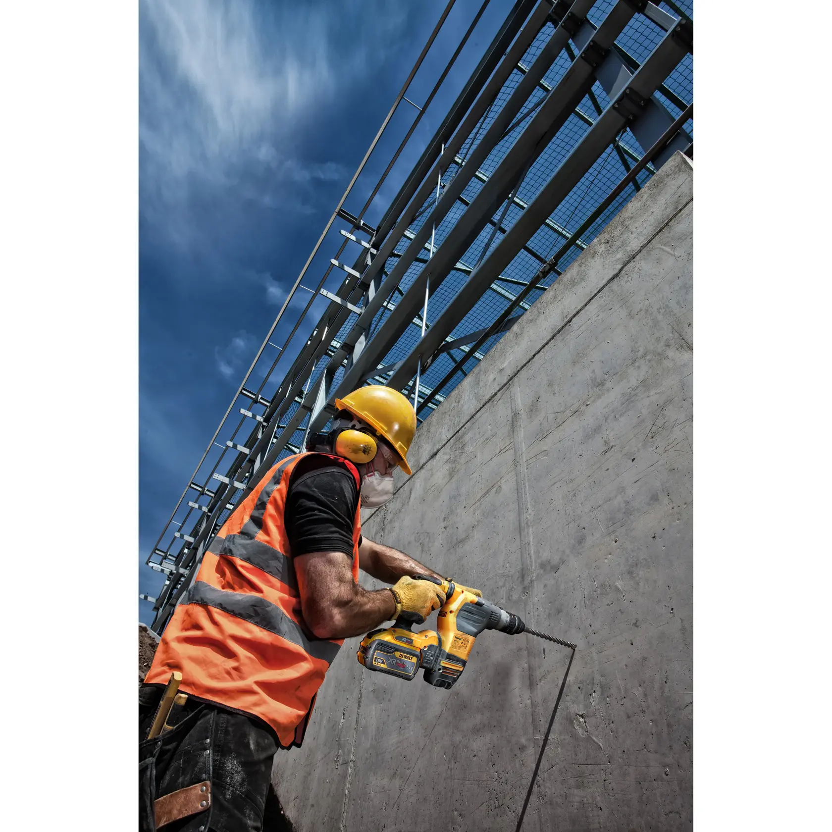 Trabajador perfora muro de concreto con herramienta DEWALT, lleva equipo de seguridad y chaleco naranja.