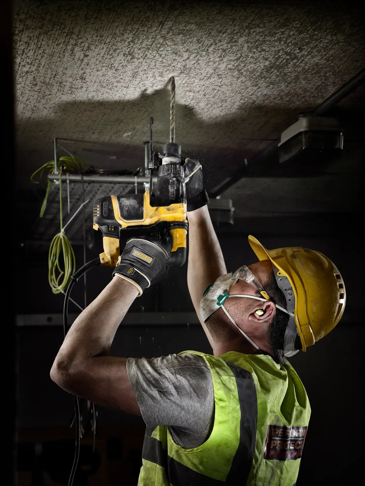Trabajador con protección usa un taladro DEWALT para hacer un agujero en el techo de la obra.