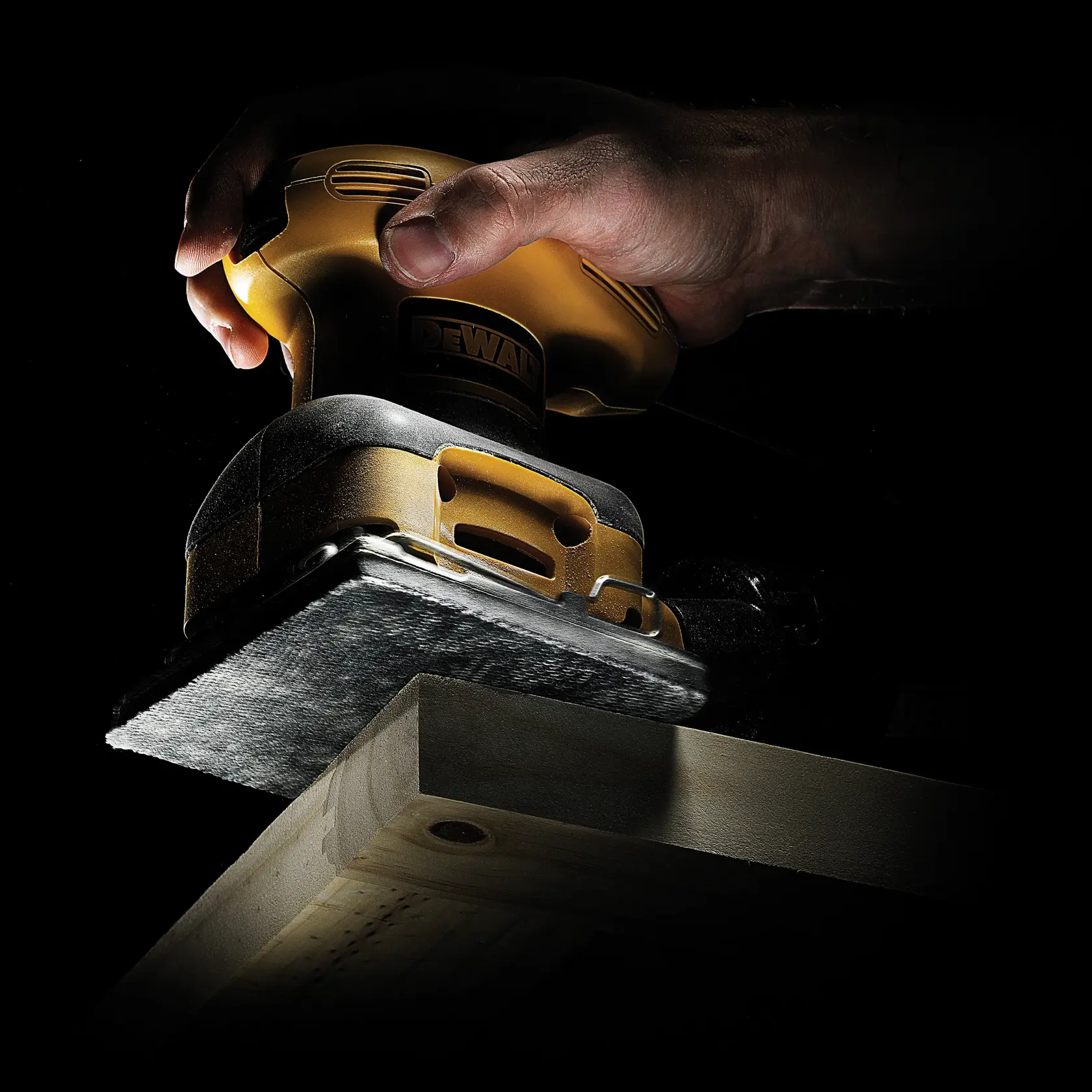 Mano usando lijadora DEWALT sobre madera, primer plano con fondo oscuro.
