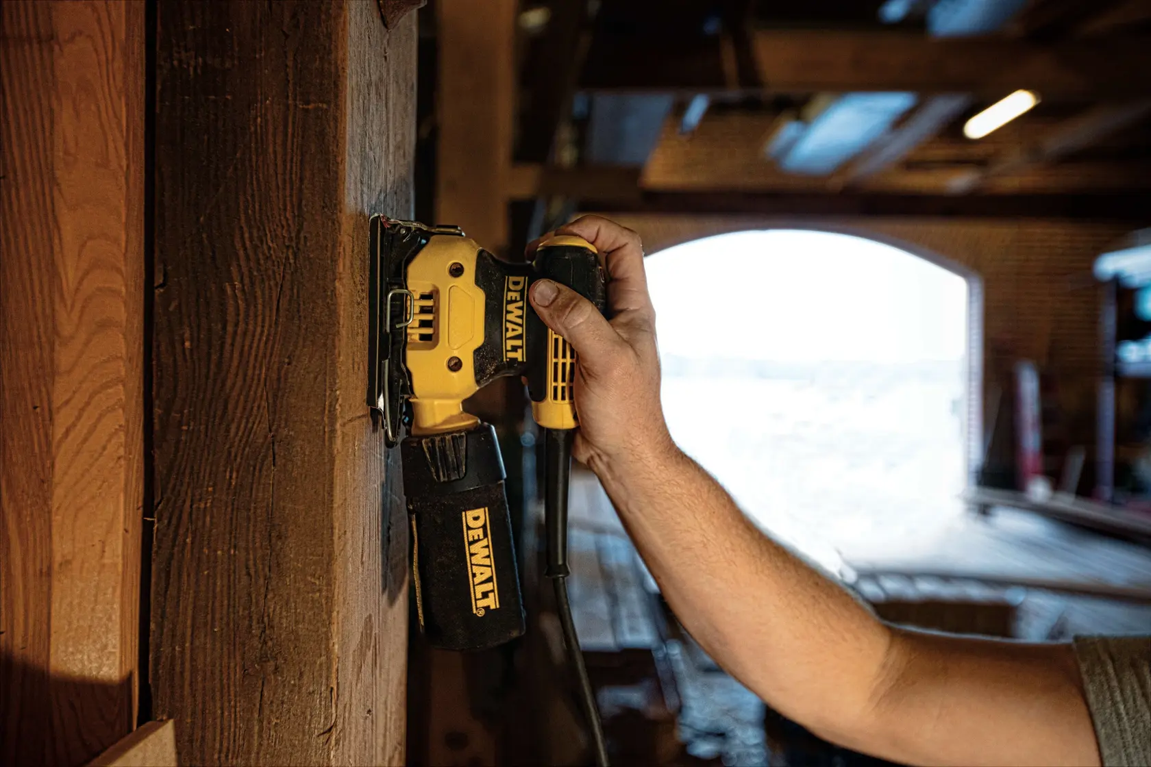 Vue en gros plan d'une ponceuse électrique DEWALT jaune et noire avec câble, conçue pour poncer des surfaces. L'outil comporte un port d'extraction de poussière et des clips métalliques pour fixer le papier de verre.