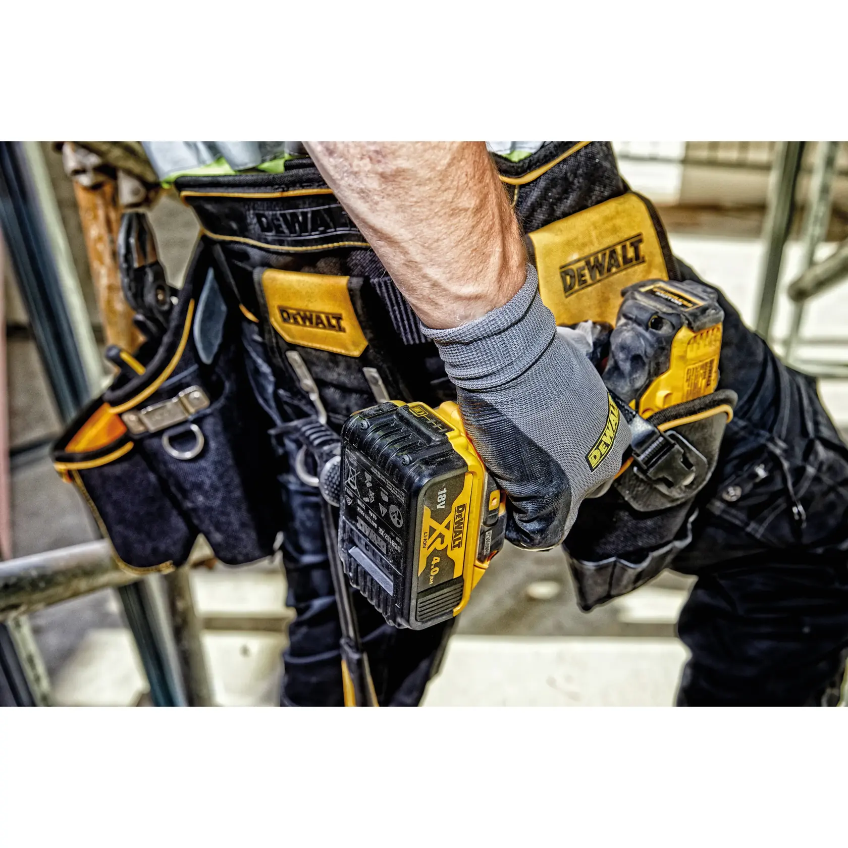 Trabajador con cinturón de herramientas y guantes DEWALT, sosteniendo un taladro amarillo DEWALT.