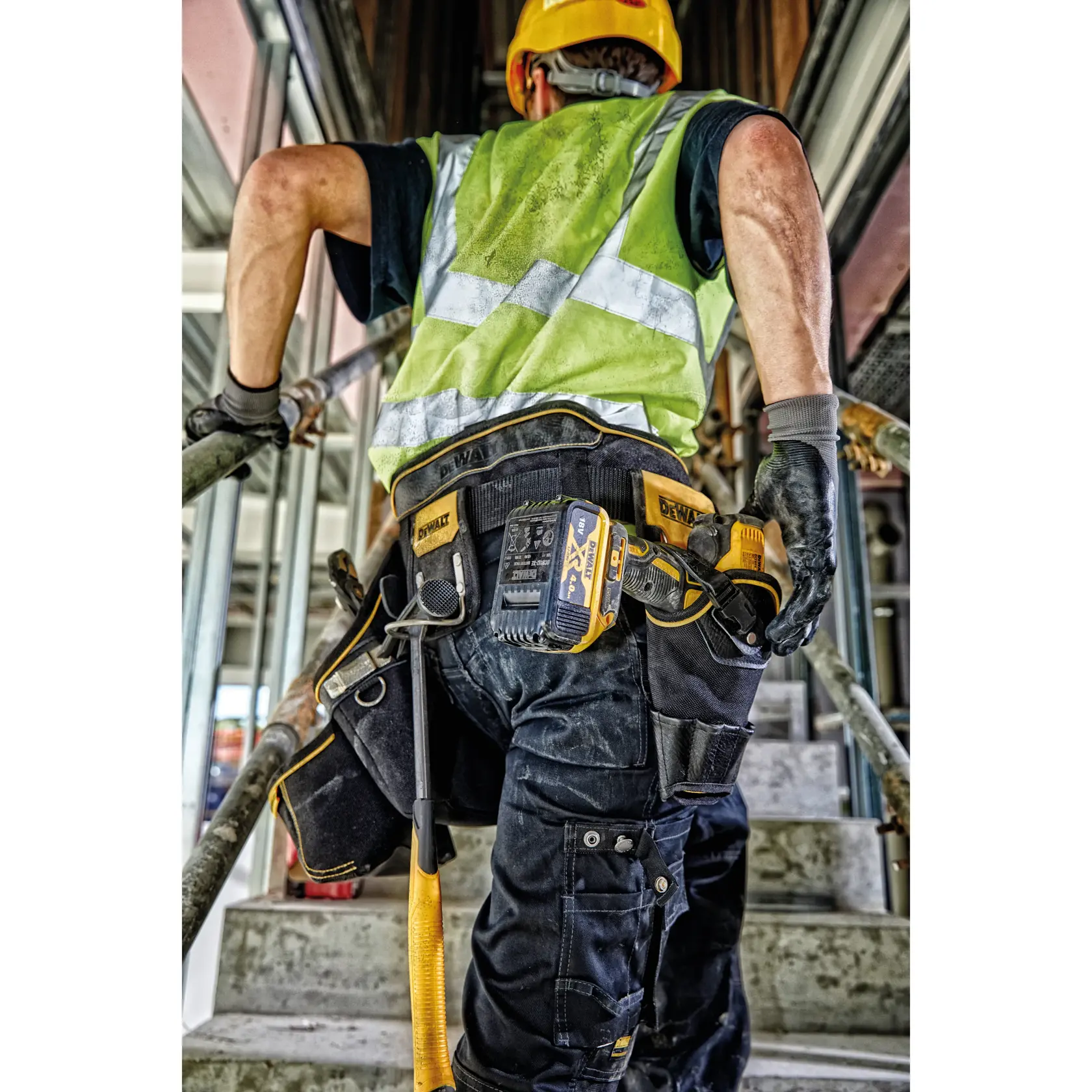 Trabajador con cinturón de herramientas DEWALT y equipo de seguridad sube escaleras en obra.