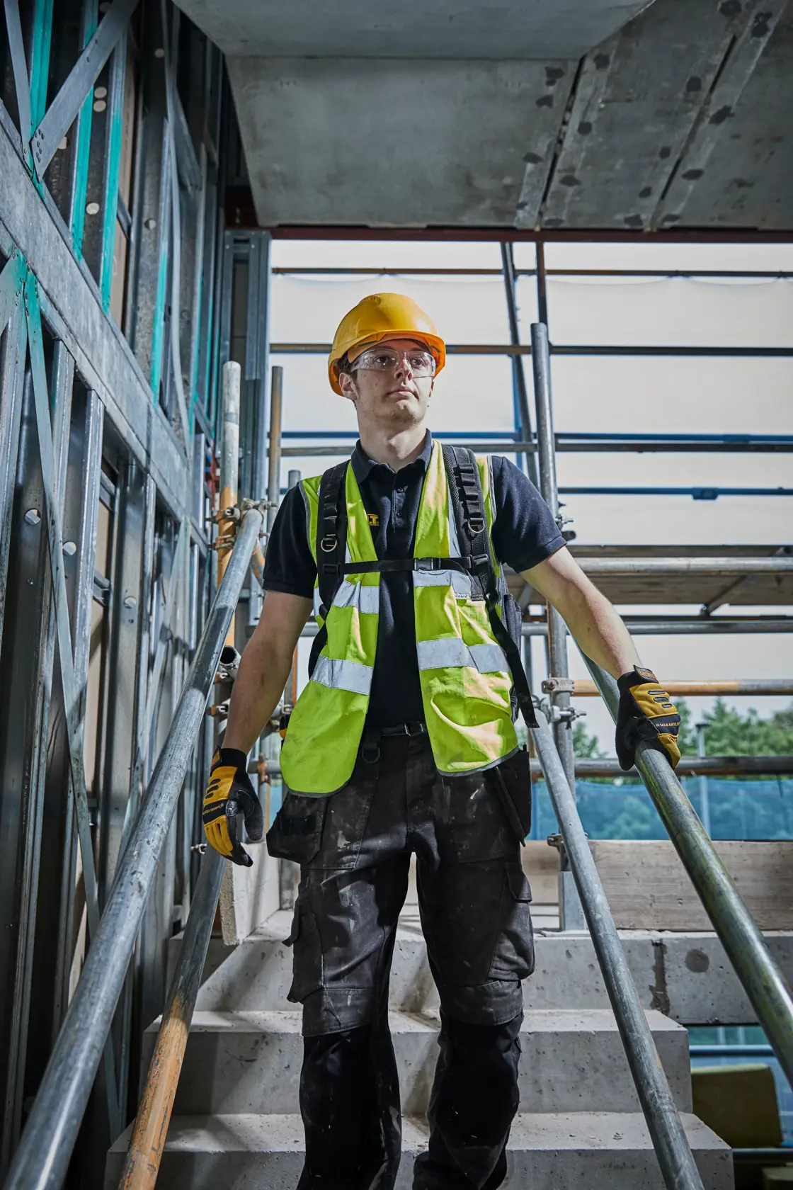 Persona con equipo de seguridad y guantes en escaleras de obra con andamio metálico.