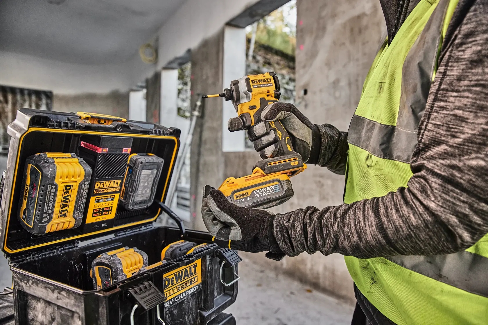 Persona con herramienta DEWALT y batería, caja y baterías DEWALT visibles en obra.