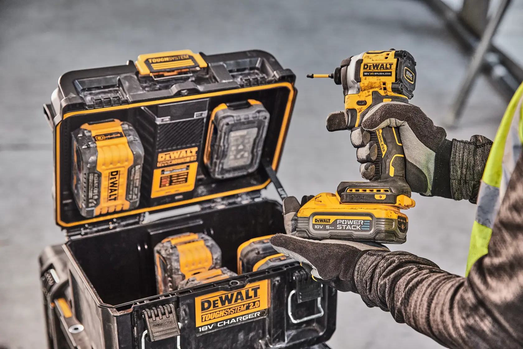 Persona sostiene taladro DEWALT, caja de carga con baterías y herramientas visible. Entorno industrial.