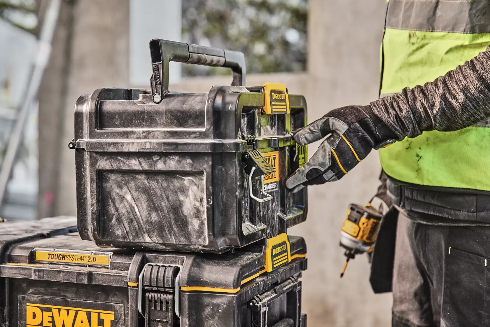 Mano enguantada abre caja DEWALT Toughsystem 2.0 apilada en un lugar de trabajo.